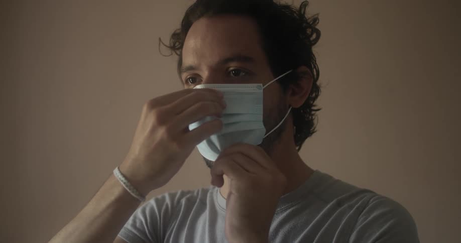 A man putting on and adjusting a medical face mask before walking off screen