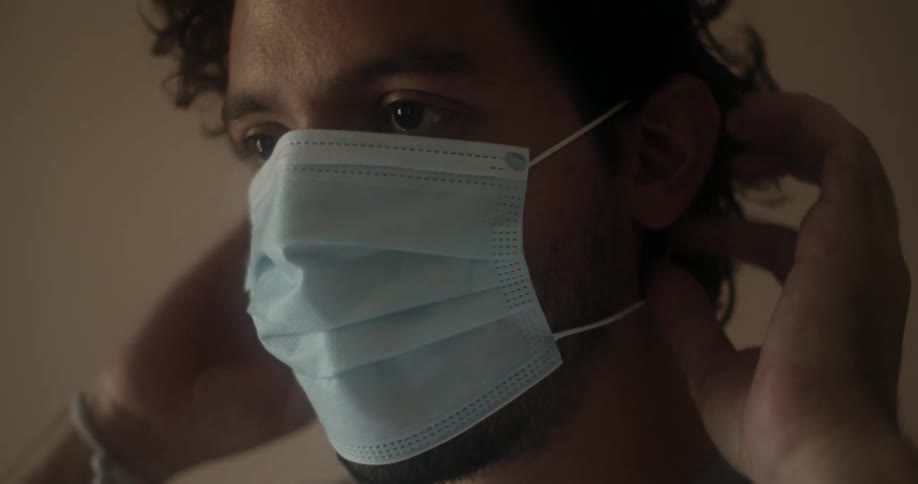 A man lifting and putting on a medical mask before walking away