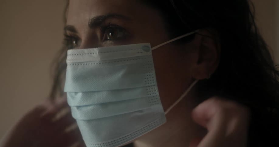 A woman putting on a medical face mask and walking out of frame