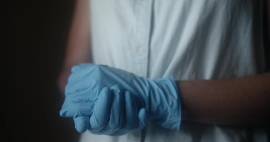 A person wearing latex gloves clasping their hands together