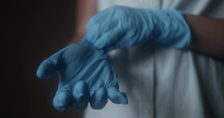 A woman pulls up the ends of the blue latex gloves on her hands