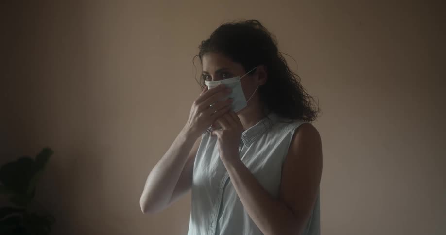 A woman demonstrates how to put on a disposable face mask