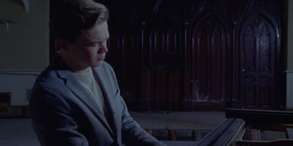 Man wearing suit plays piano in dimly lit room