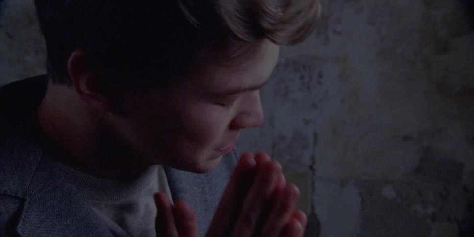 A man anxiously rubs his face and runs his hand through his hair while standing next to a distressed wall