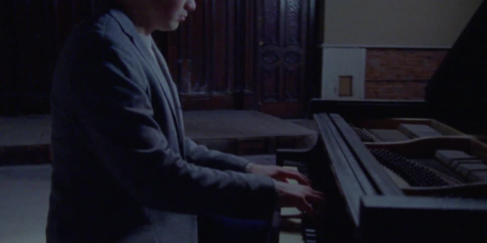 A man plays piano in a dark theater