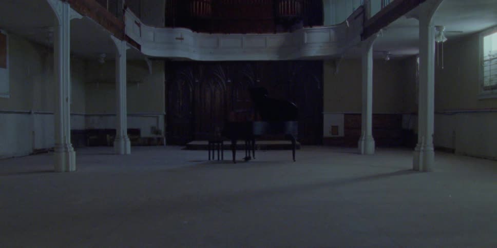 A black grand piano sits in a large empty room of an abandoned building