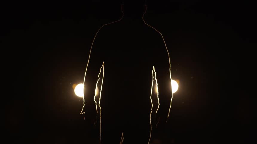 A man walks towards a car's headlights at night