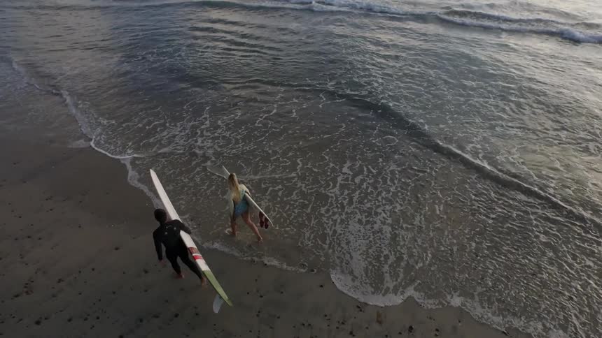 Two people holding surfboards walking along the beach