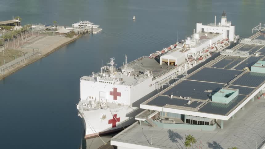 A red cross ship is moored at a dock