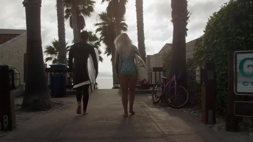 A man and woman holding surfboards are walking towards the water