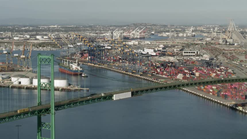 A freighter moves past city and tanks near bridge