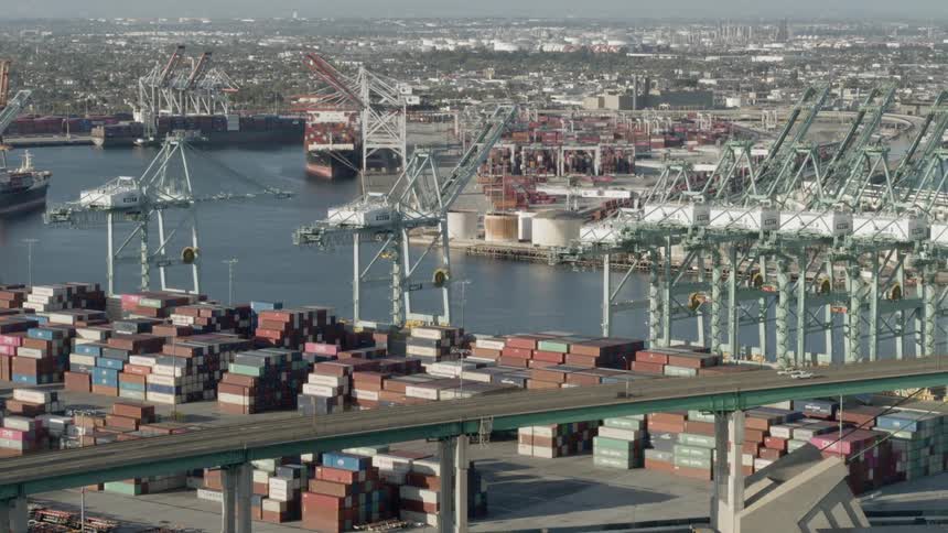 Cars drive over a bridge near a shipping port