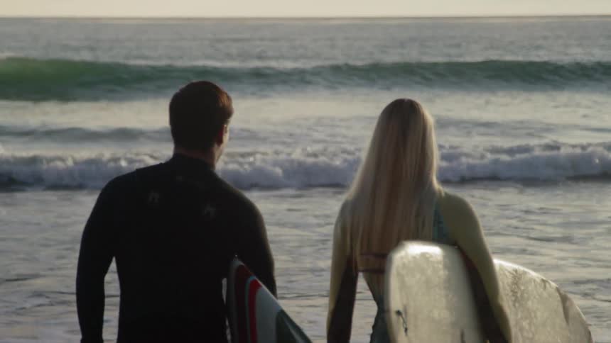 Man and woman carrying surfboards walk into the ocean
