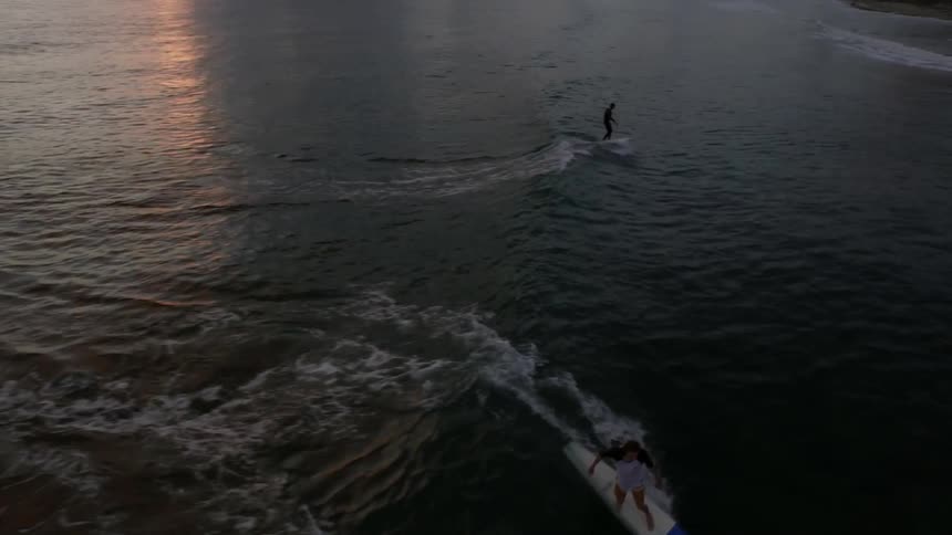 Surfers catch and ride a wave to shore at sunset