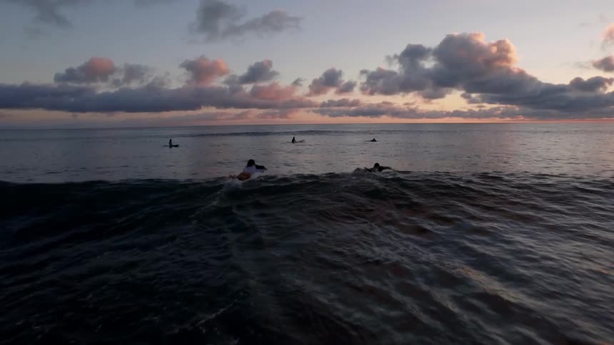 Two surfers paddle out to join others at sunset