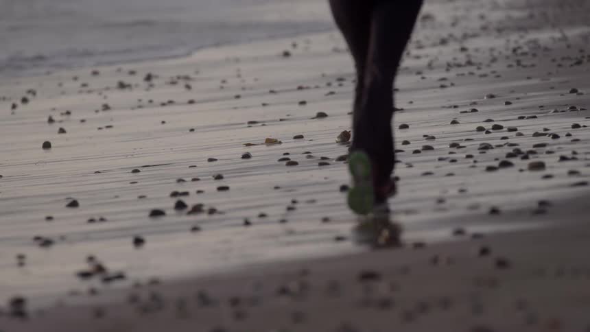 A woman jogging on beach with scattered rocks