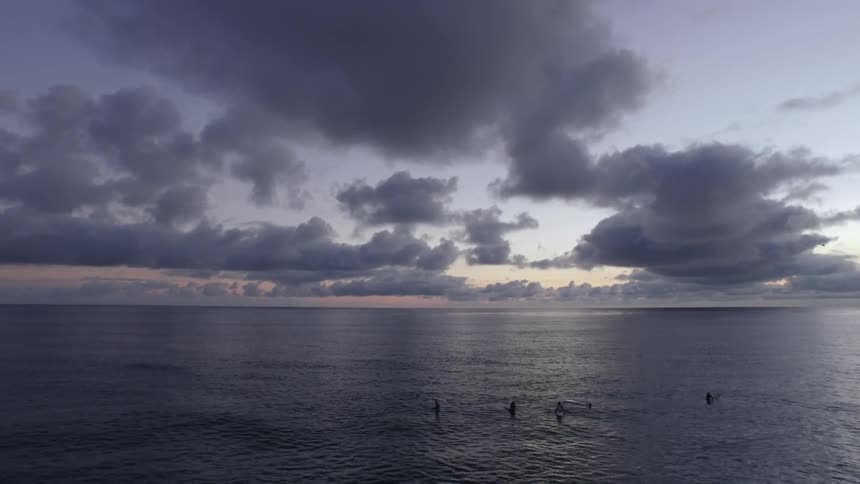Five surfers relax in the water as sun sets