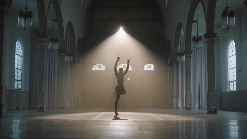 A male dancer dances by himself in a large open cathedral room