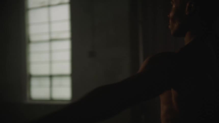 Shirtless african american male dancer moves and follows a set sequence of steps in a dim room