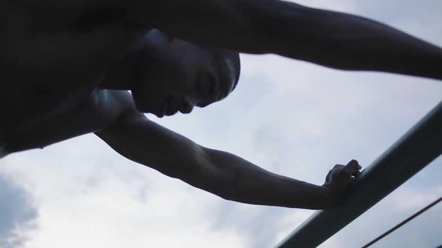 A man without a shirt holding onto a handrail with the sky above
