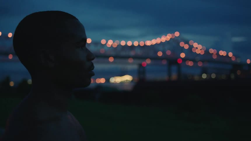 A man stands in front of a city bridge at night