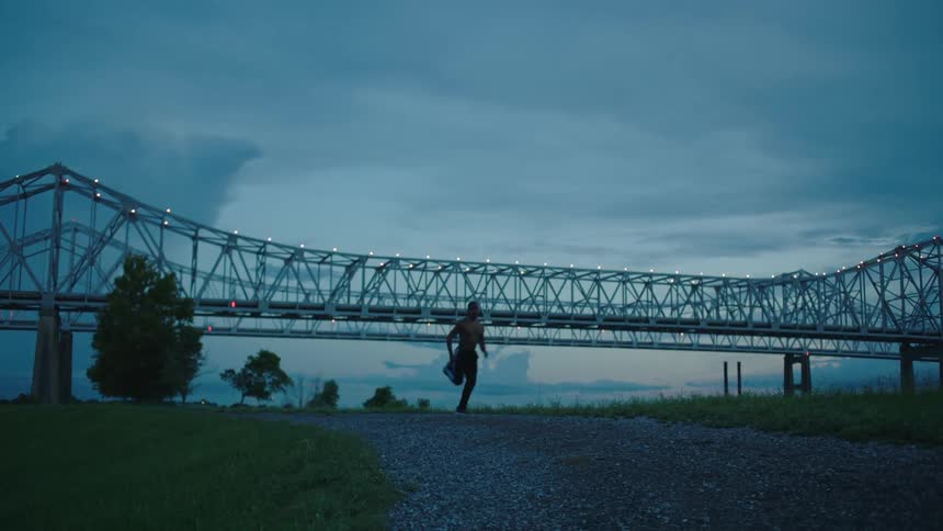 A runner passes in front of a bridge at night