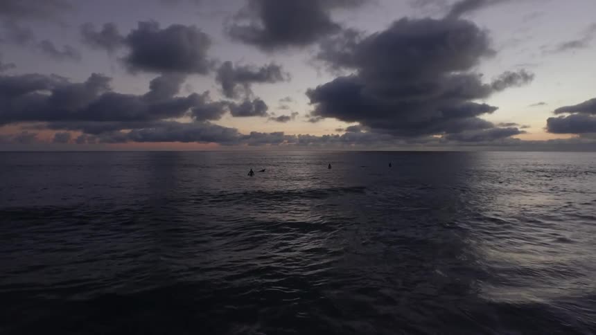 People are surfing in the water as the sun sets