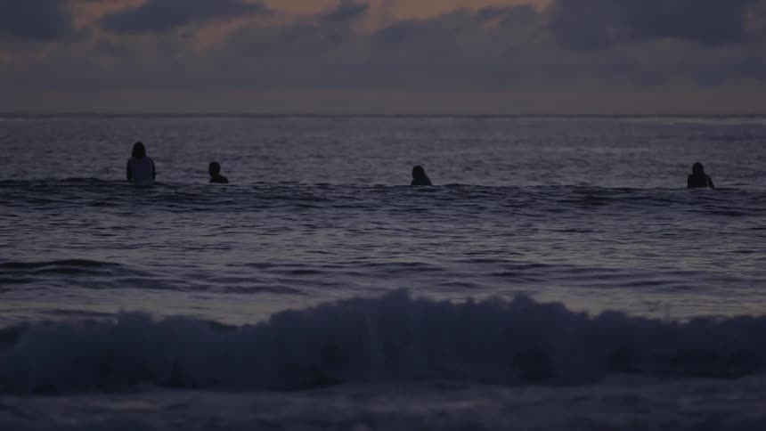 Surfers sit on their boards in the ocean at sunset