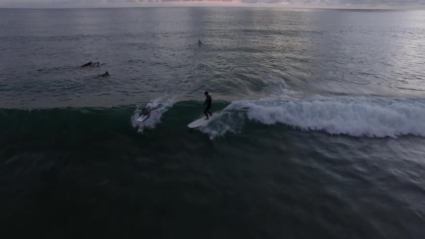Surfers ride a wave in the ocean on a cloudy morning