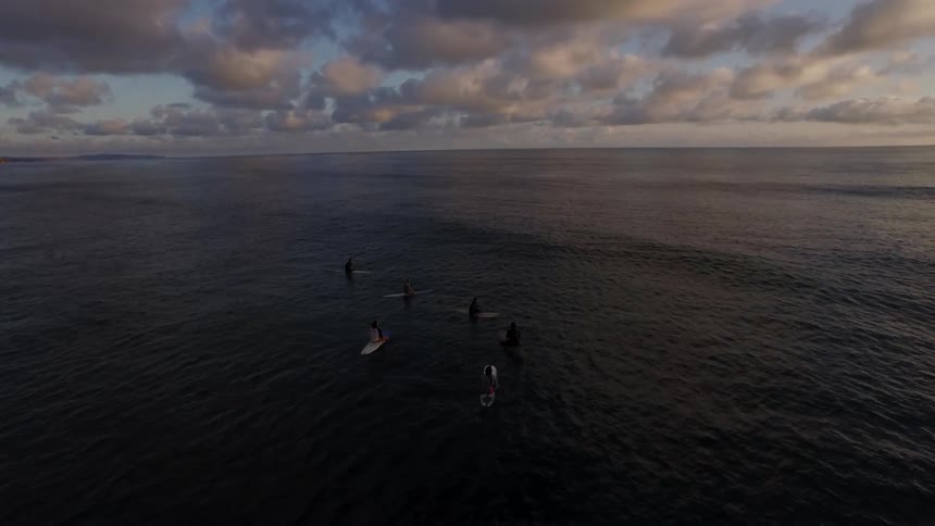 People on surfboards paddle out into the ocean at dawn