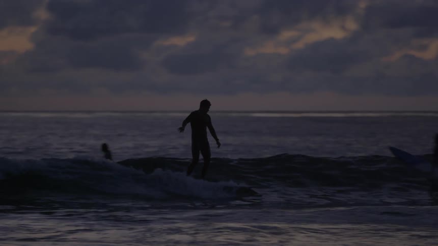 People are surfing in the water at sunset