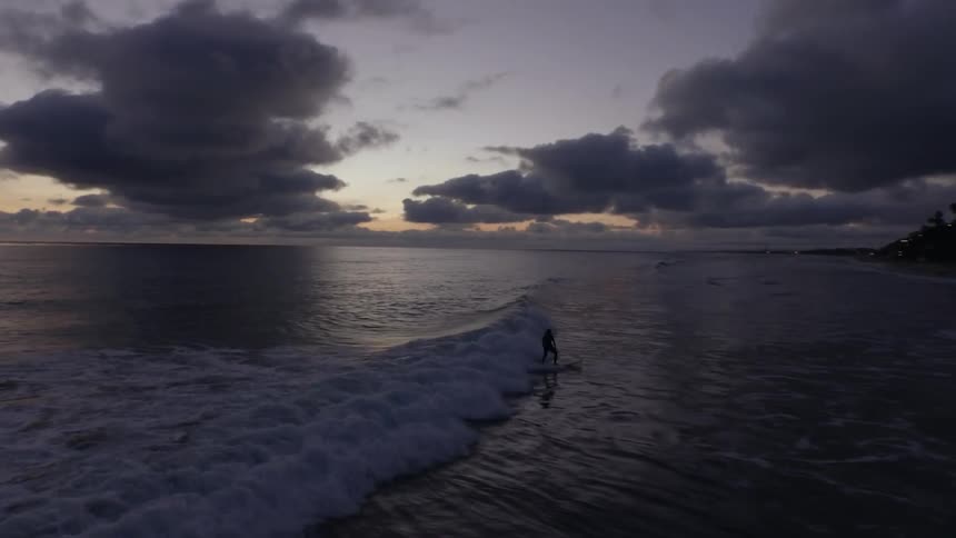 People surf a wave in the ocean on a cloudy morning