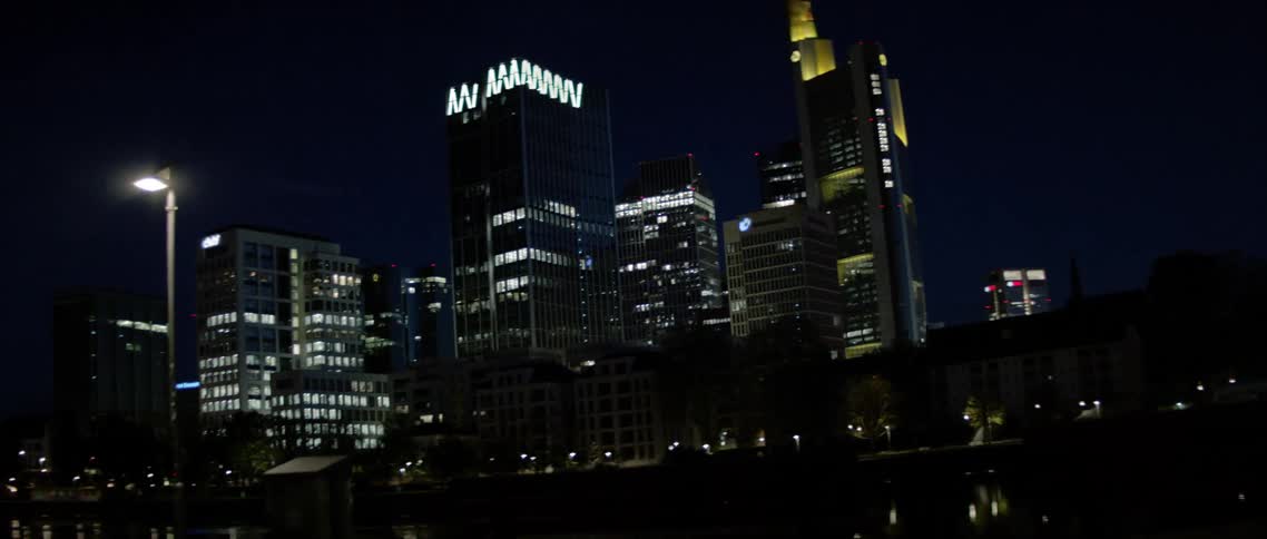 City building lights shine and glow at night reflecting off the surface of the water in a park