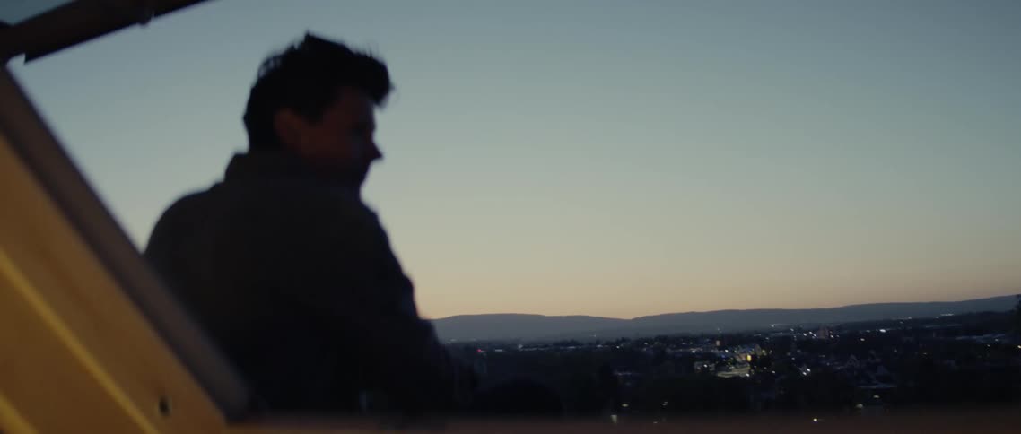 A mans silhouette sitting on the roof watches the cityscape at dusk