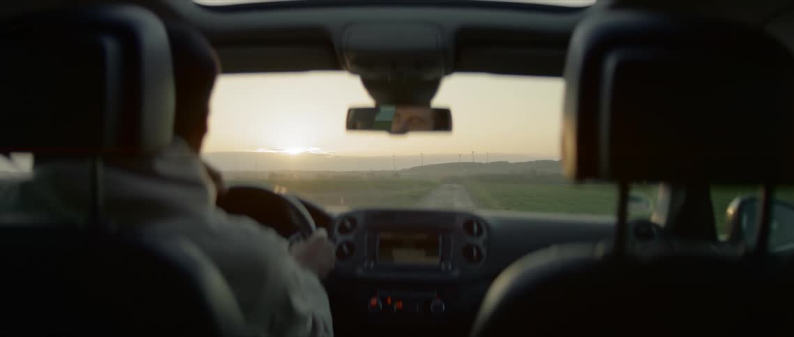 A man drives down a rural two lane road as the sun rises