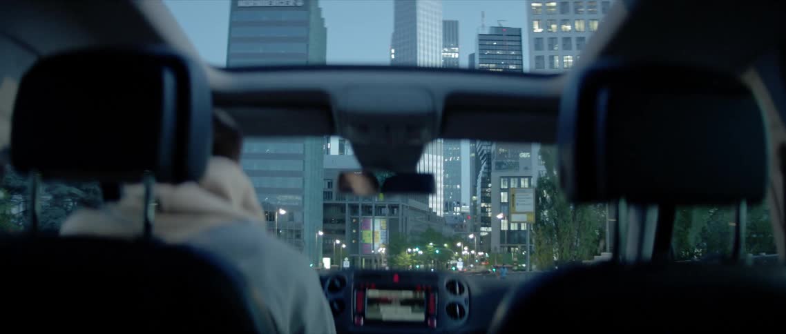 A person driving a vehicle with a sun roof through a metropolis in the evening