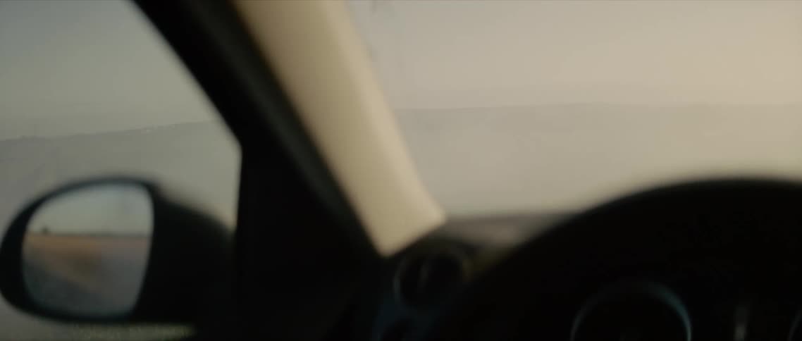 Looking through the window and windshield of a car parked in a grassy field surrounded by fog