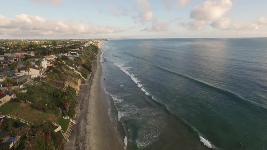 Houses sit on steep hill with waves crashing on beach below