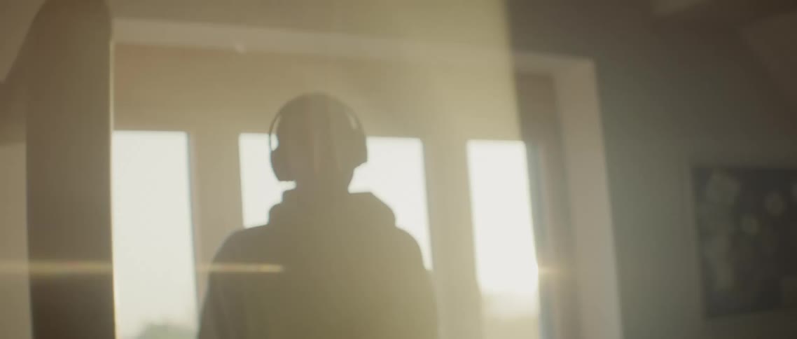A teenager with headphones on walks in to a house