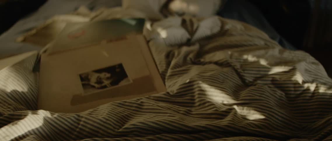 A man picks a set of wireless headphones up off his bed to listen to the record playing on the stereo