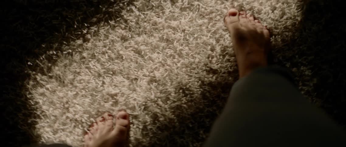 A man walks barefoot on an area rug stepping from dark and shadows into sunlight