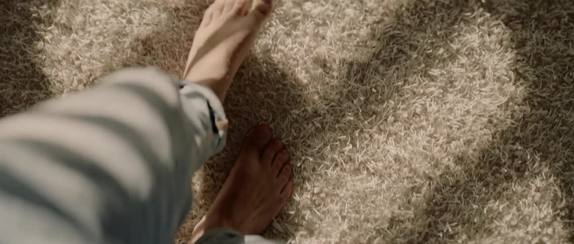A man with bare feet walks on a rug stretching his toes in the sunlight shining down on it