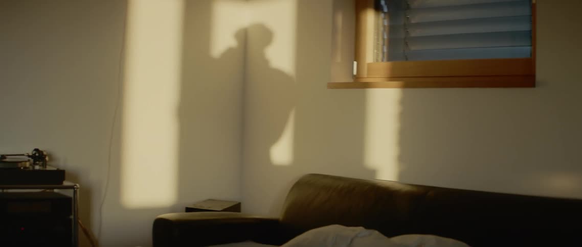 The shadow of a person swaying to music is cast on the wall above a sofa bed and stereo