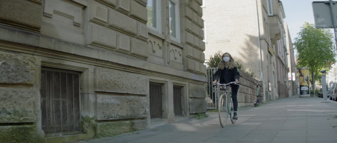 Blonde girl wearing a white face mask rides a bike on the pavement in the city