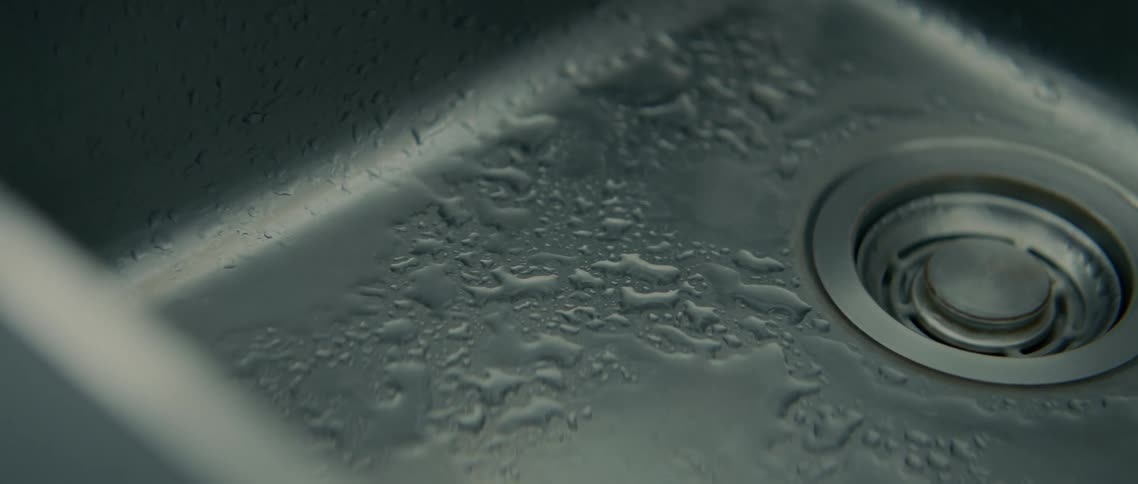 Water drips from a faucet into a stainless steel sink