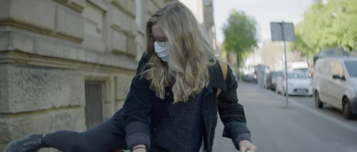 Blonde woman wearing a white face mask gets on a bicycle in the empty street during coronavirus pandemic