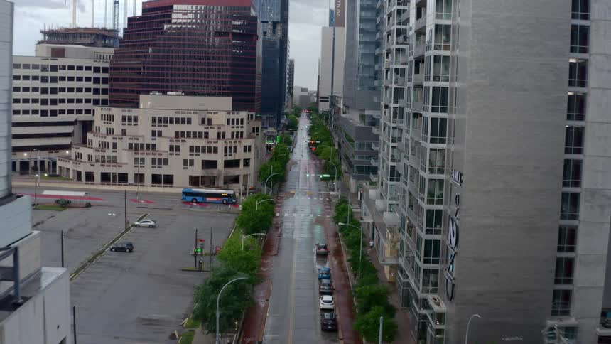 An empty street with a few cars in a lot in a large city downtown area on a rainy day
