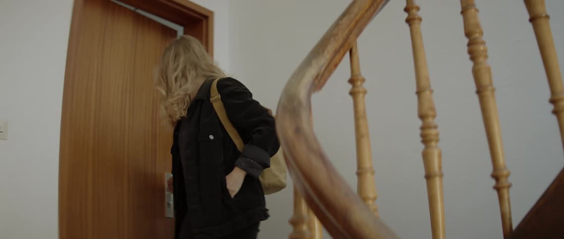 A woman with a face mask opening a door then walking down a staircase