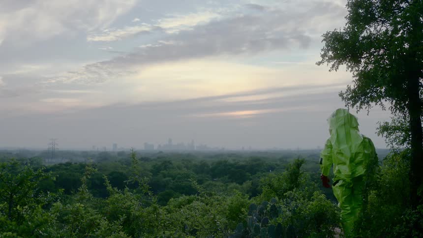 A person in a hazmat suit walks towards a city