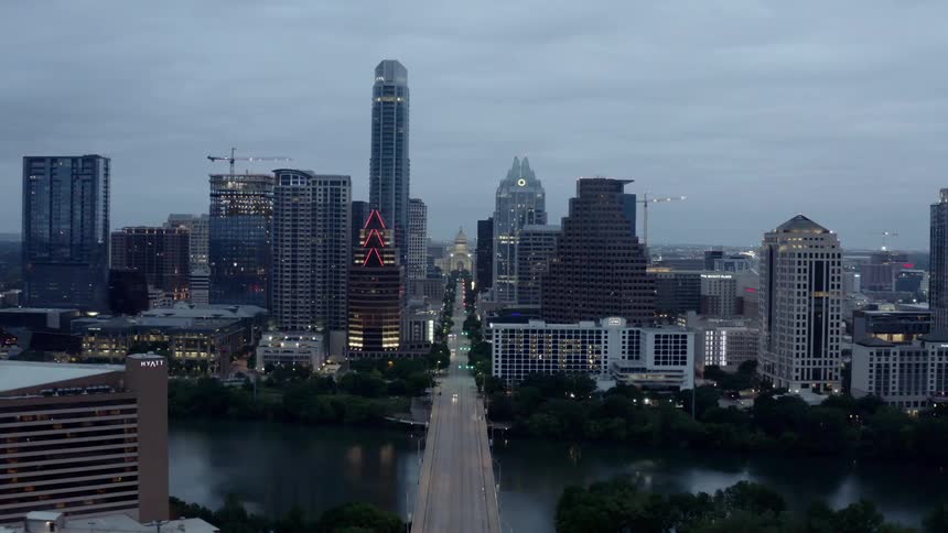 A wide bridge over a river leading into a metropolis in the evening
